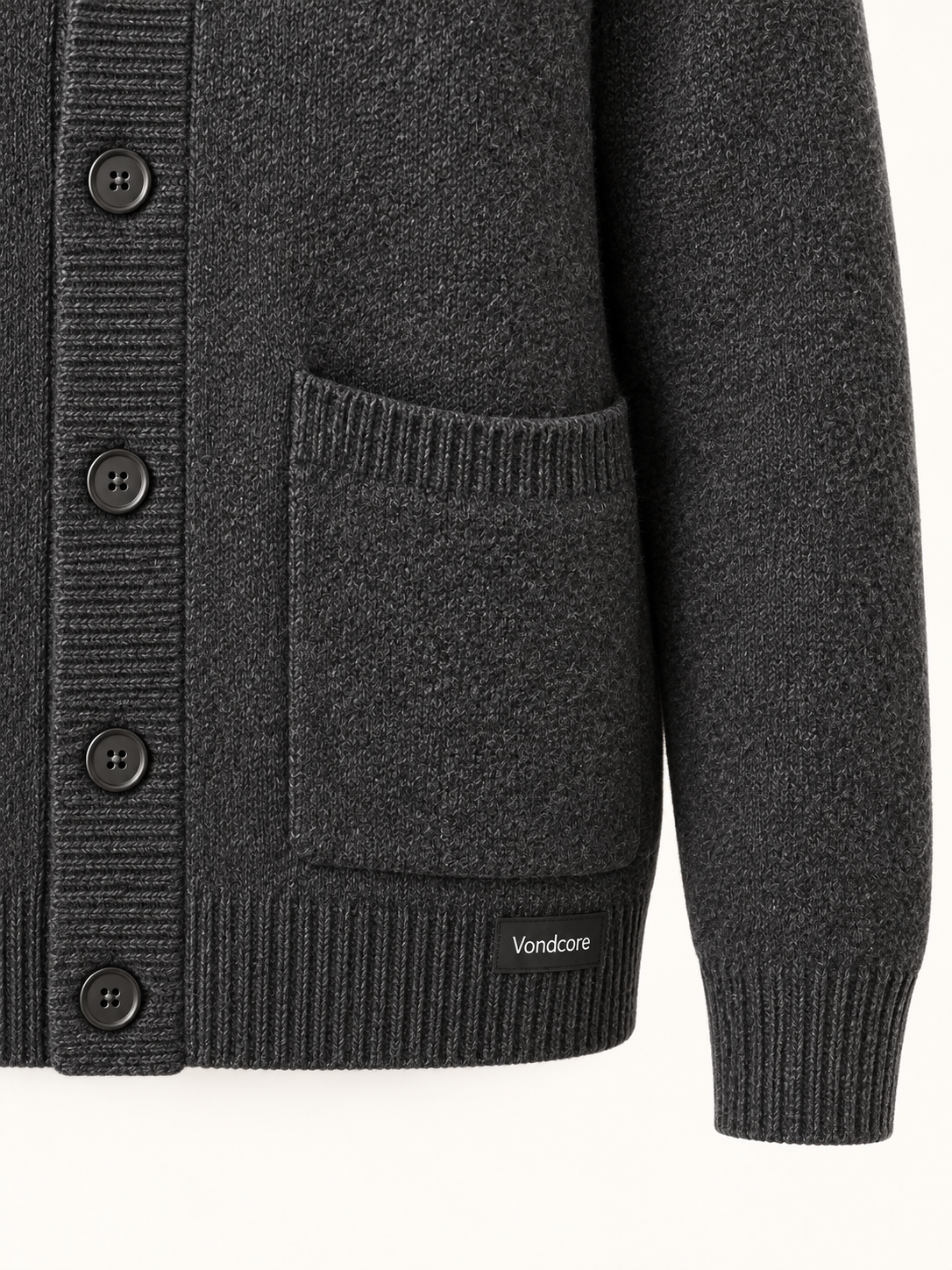 Detail of the charcoal Vondcore Ember Shawl Cardigan showing knit texture, patch pocket, button and Vondcore hem label.